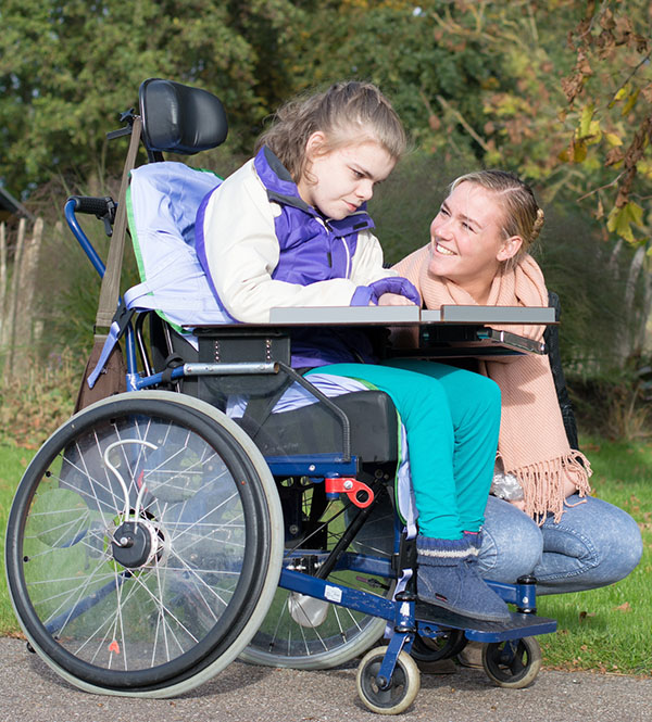 A disabled child in a wheelchair relaxing outside together with a care worker