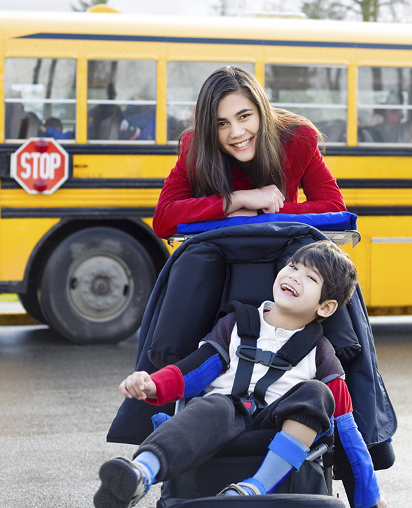 Teacher with disabled boy in wheelchair by school bus